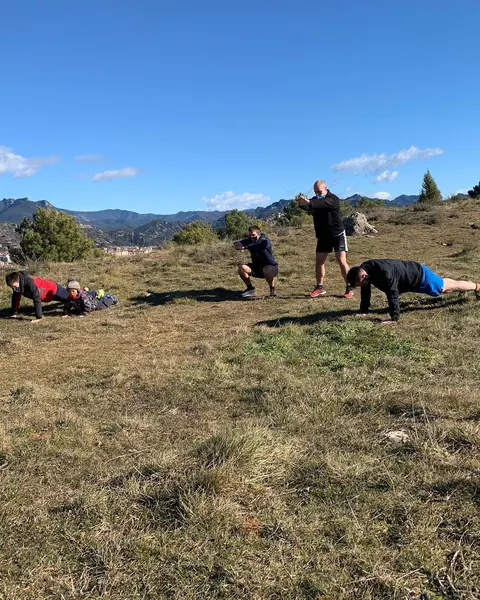 Quatre persones fent exercicis a l'herba, a la muntanya, un dia de cel blau