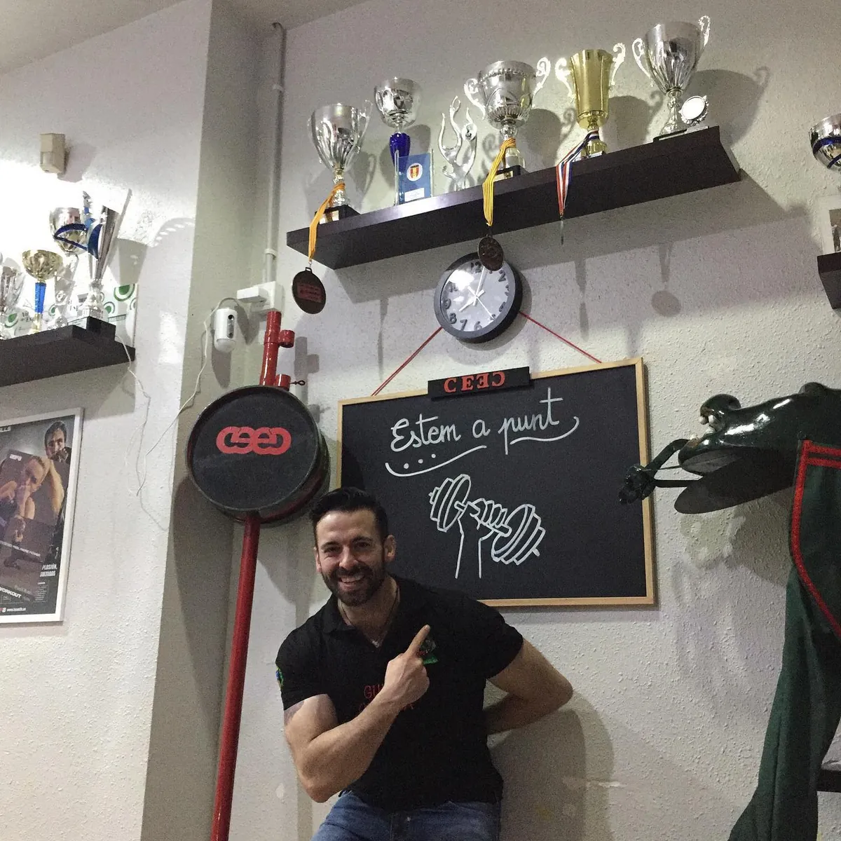 Mario Erra somrient a la recepció del CEEC, al costat de la pissarra i dels trofeus